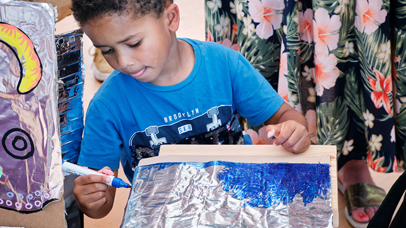 A boy colouring tinfoil with blue pen
