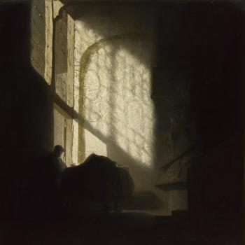 A Man seated reading at a Table in a Lofty Room