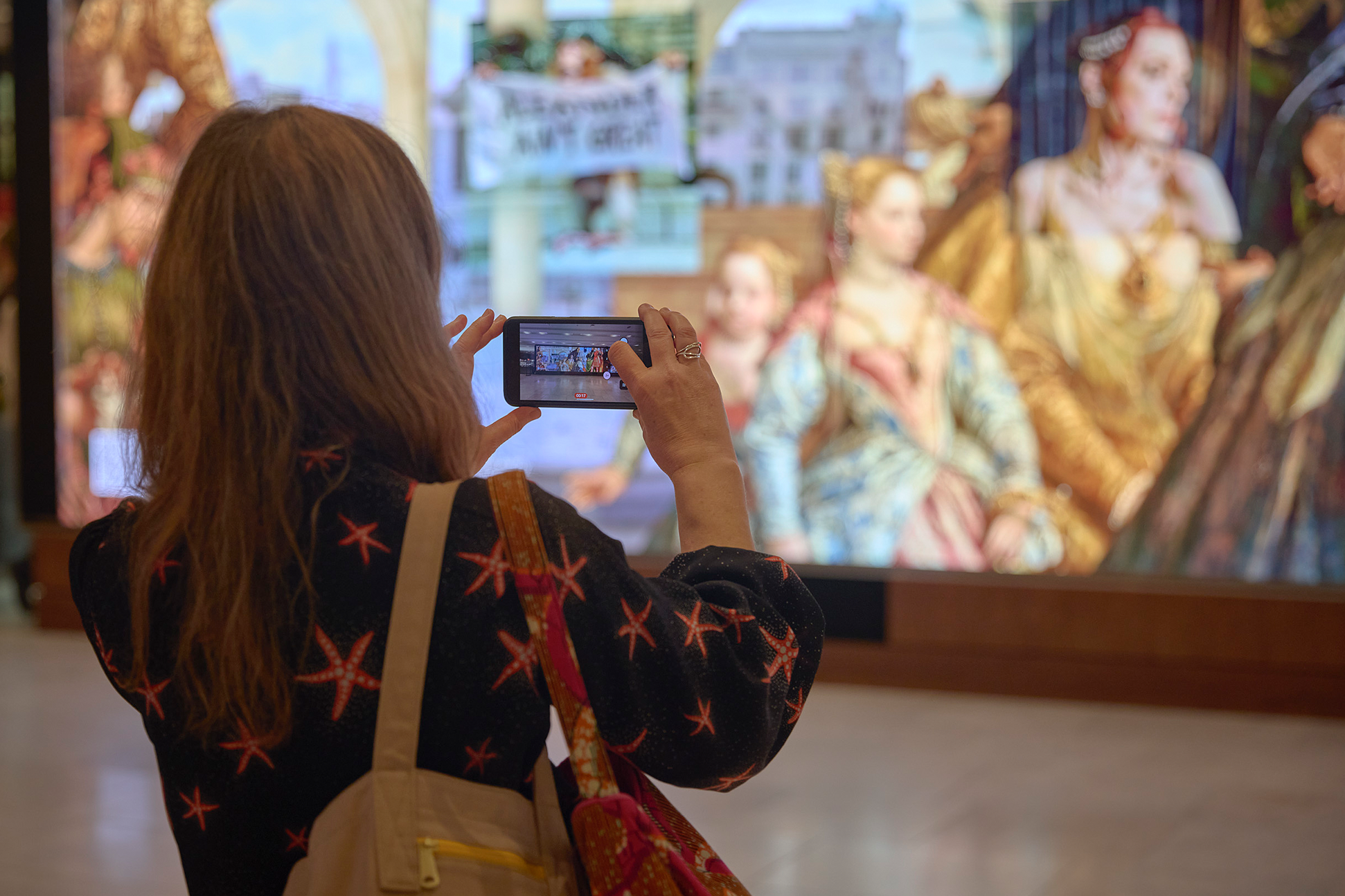 A visitor watches the Community Connector film on the Big Screen in the Sainsbury Wing in the National Gallery.